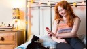 woman on phone in bed with cat next to her